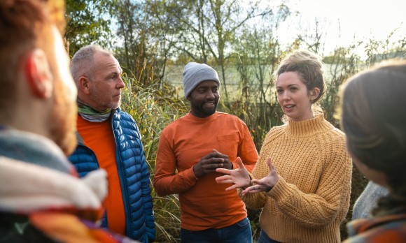 A multiracial group of volunteers wearing warm casual clothing and accessories on a sunny cold winters day. They are talking before they start working on a community farm, planting trees and performing other tasks.